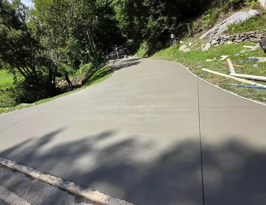 New concrete driveway with control joints beside a stone and boulder wall