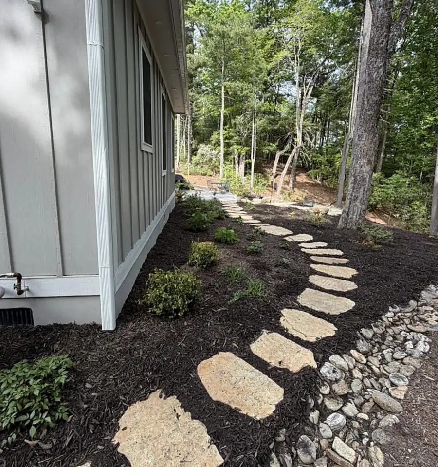 Flagstone steppers through dark mulch beside a grey house with a river-rock swale