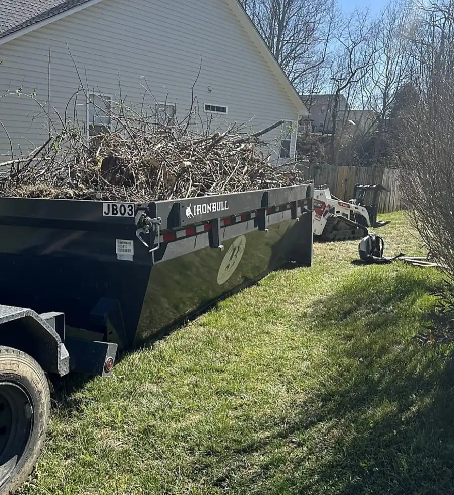 Black roll-off bin full of brush and limbs with a mini track loader behind
